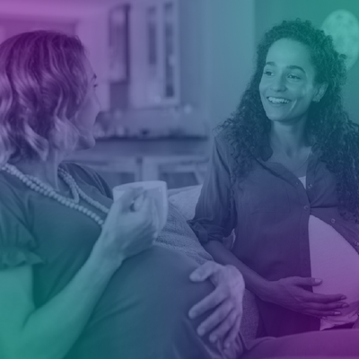 Two women chatting on a couch, one holding a mug, in a softly lit home setting with a blue-purple tint.