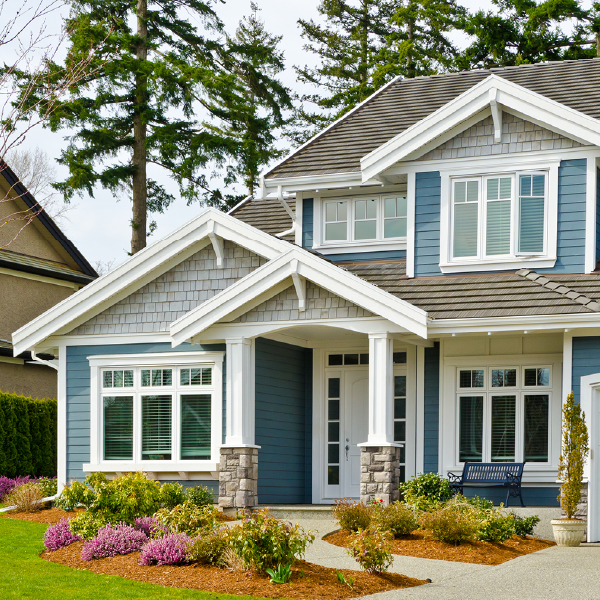 Suburban house with blue siding, white trim, stone columns, and colorful front landscaping