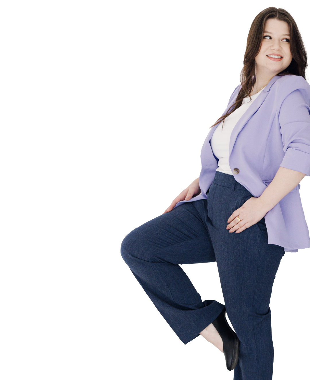 Woman standing in a lavender blazer and dark jeans on a white background, one leg raised and smiling.