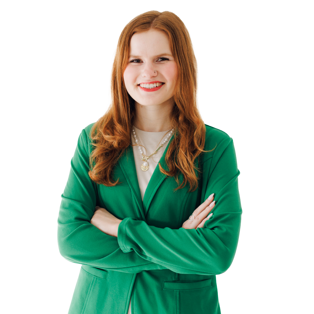 Smiling woman with red hair in a green blazer, standing with arms crossed against a white background