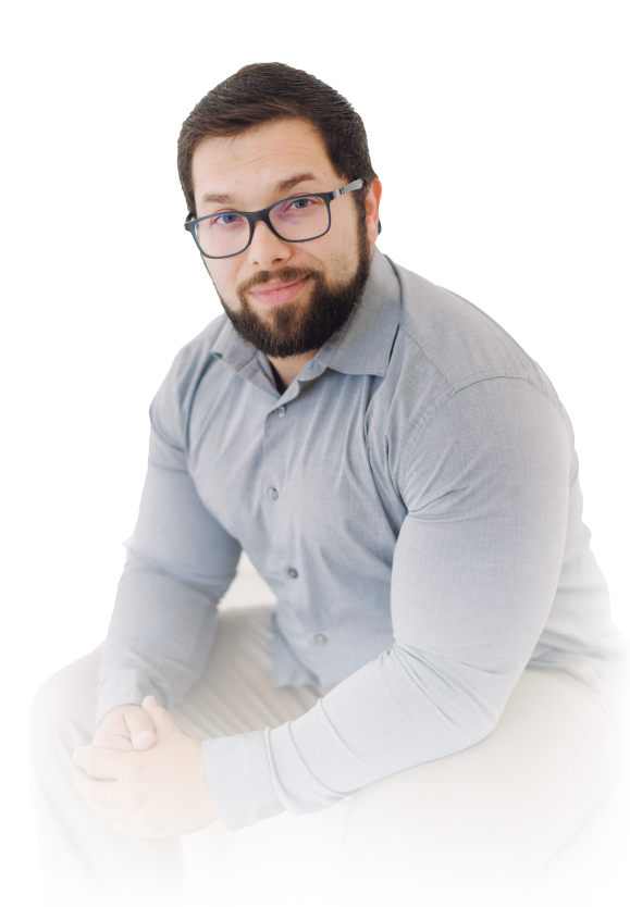 Man seated against a white background, wearing glasses and a light gray shirt, looking at the camera