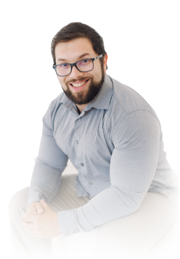 Smiling person with glasses and beard, seated in a light gray shirt against a white background