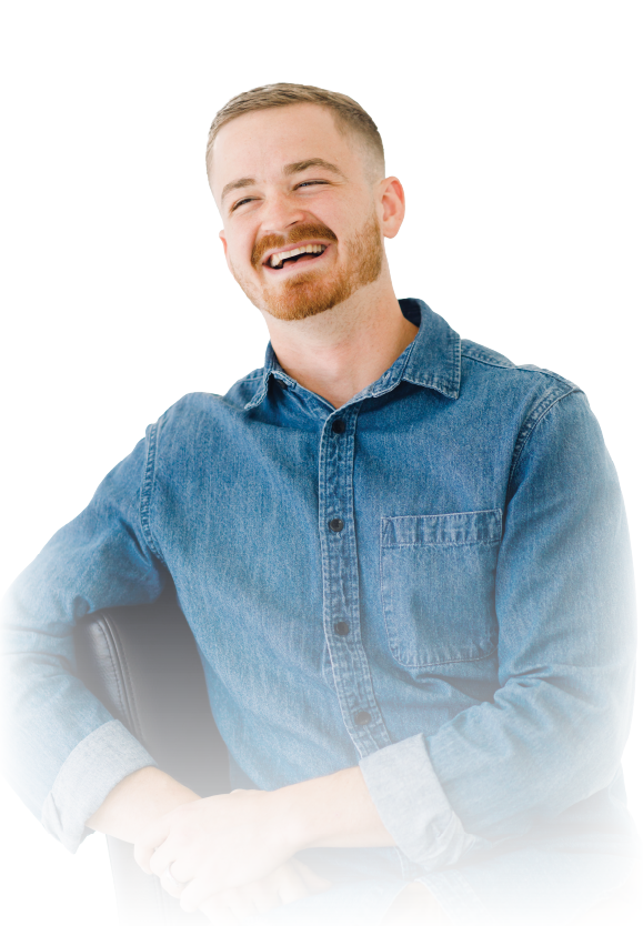 Smiling man in a blue denim shirt sitting with folded hands against a white background