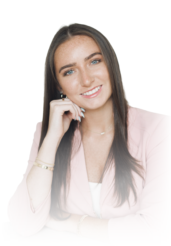 Smiling woman in a light pink blazer with long brown hair, resting her chin on her hand against a white background