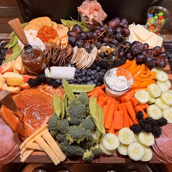 Charcuterie board with salmon, grapes, crackers, cheese, veggies, berries, and dips arranged on a platter