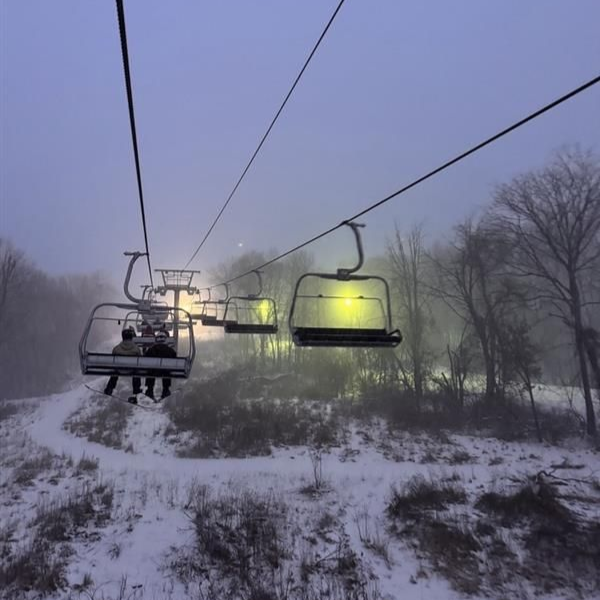 Snowy ski lift chairs moving through a foggy winter landscape at dusk