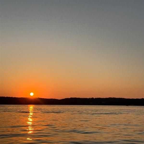 Sunset over calm water with orange reflection and silhouetted shoreline