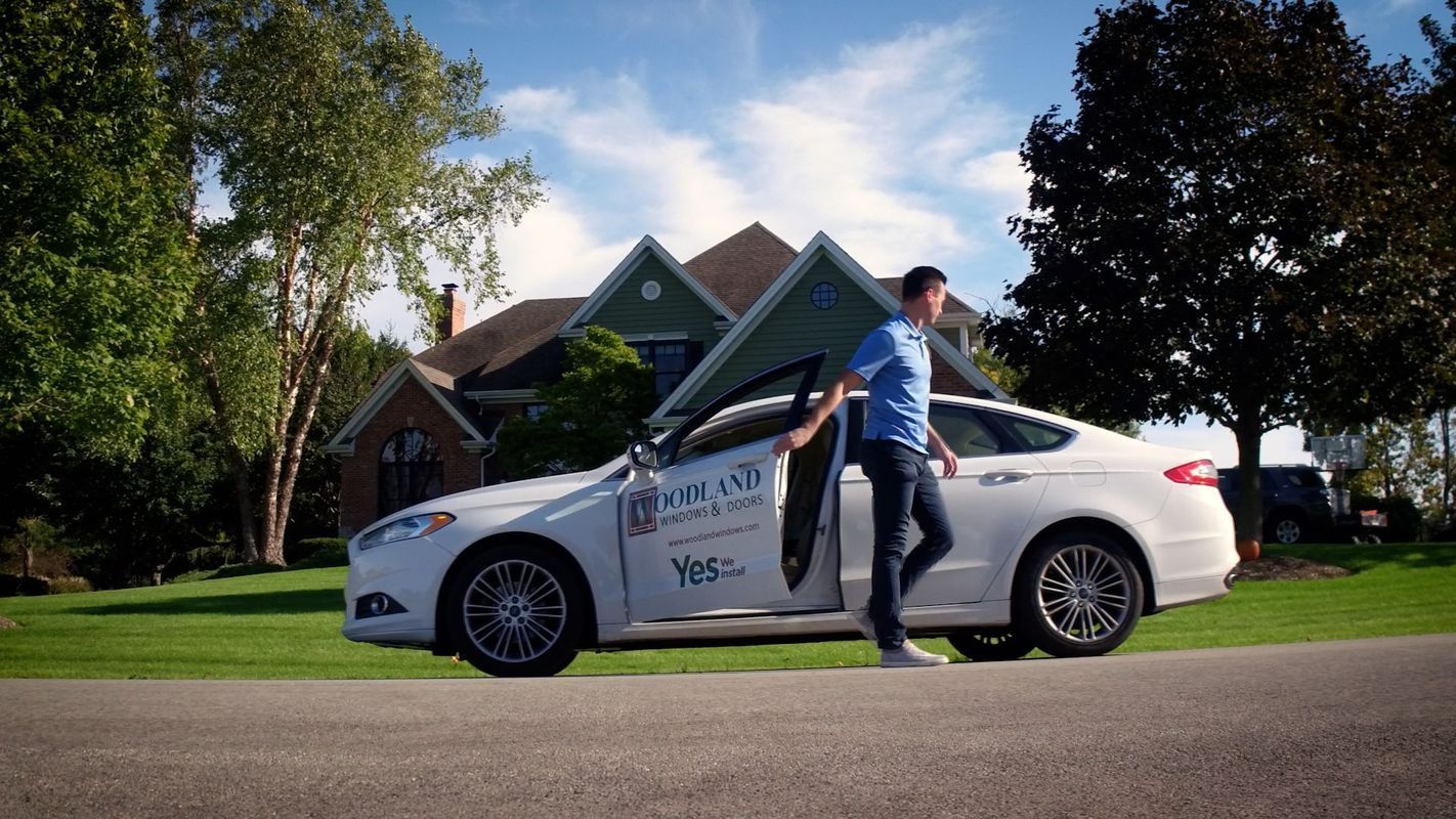 White sedan with a man stepping out, parked in front of a house on a sunny suburban street