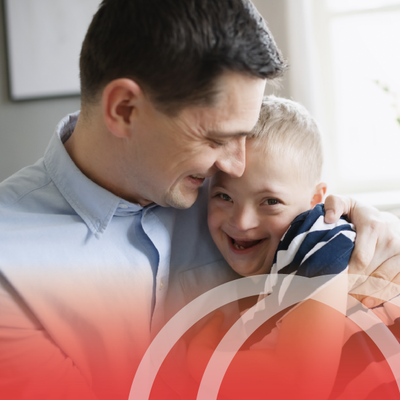 Smiling man hugs a laughing child indoors near a bright window
