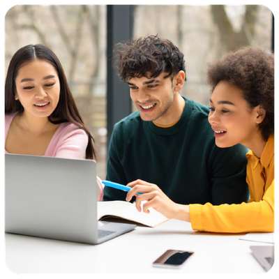 Three people smiling and collaborating around a laptop at a table with notebooks and a phone