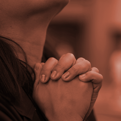 Hands clasped in prayer in warm, dim light.