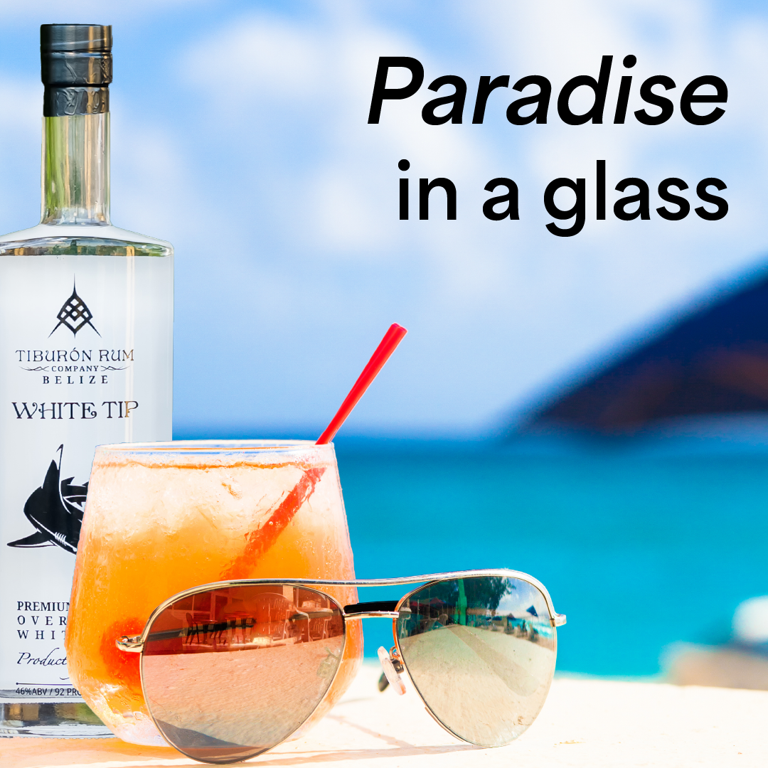 A tropical drink beside sunglasses and a bottle, with “Paradise in a glass” text on a beach background