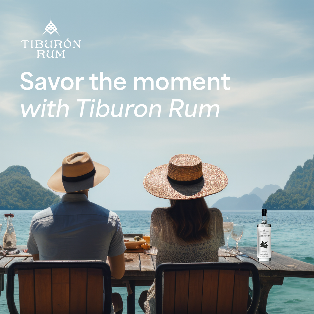 Two people sit by the sea at sunset with Tiburon Rum bottles and text reading “Savor the moment with Tiburon Rum”