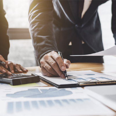 Businessperson reviewing documents and signing papers at a desk with a calculator and charts.