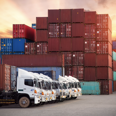 White delivery trucks parked in front of stacked shipping containers at a freight yard