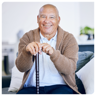 Smiling man sitting on a couch, holding a cane, in a bright living room.