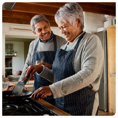 Two people smiling while cooking together in a kitchen, stirring food in a pan on the stove.
