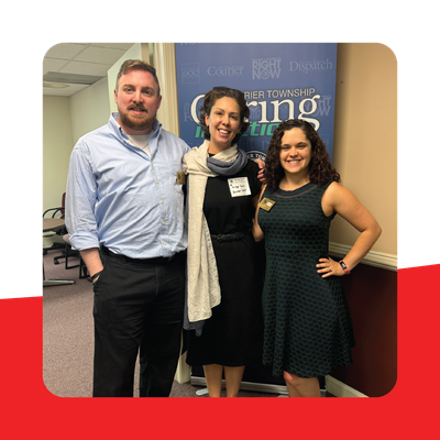 Three people posing indoors at a networking event in front of a blue conference banner.