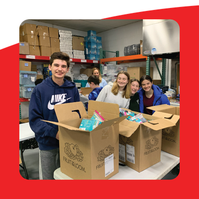 Volunteers packing donation boxes in a warehouse, with smiling people around a table