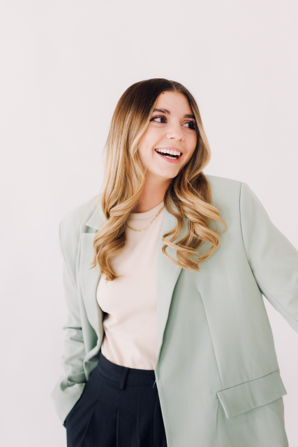 Smiling person in a mint blazer and beige top against a light background