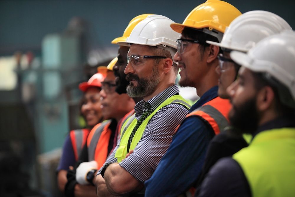 Workers in hard hats and safety vests standing in a row at an industrial site