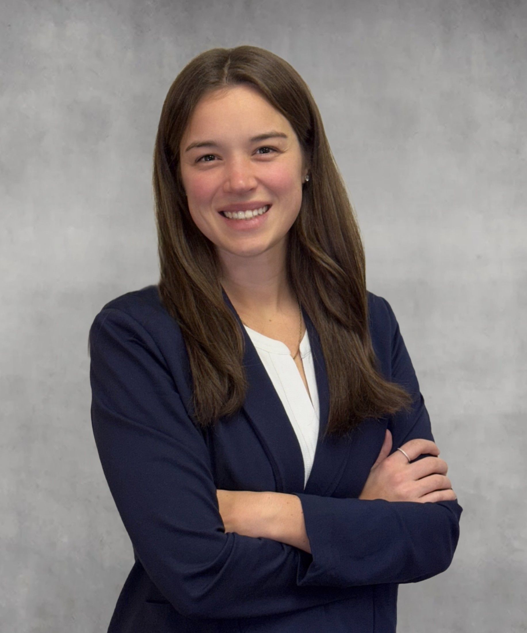 Woman in a navy blazer, arms crossed, smiling. Against a gray background.