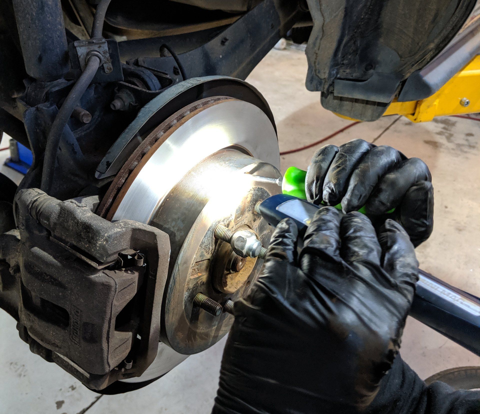 A person wearing black gloves is working on a car brake