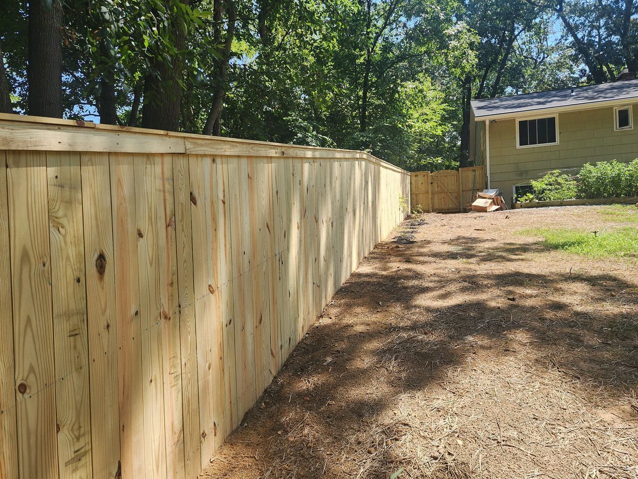 A wooden fence surrounds a dirt path leading to a house.