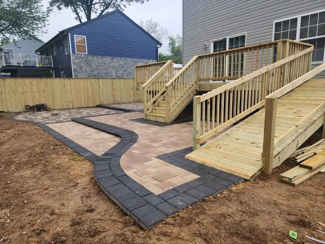 Wooden deck with stairs and a ramp, surrounded by a brick patio and a wooden fence. All built by J Gonzalez