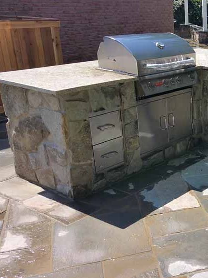 A stainless steel grill is sitting on top of a stone island.