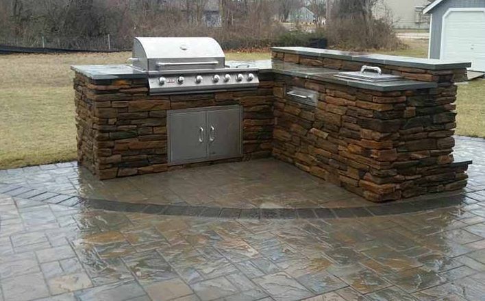 A grill is sitting on top of a stone counter on a patio.