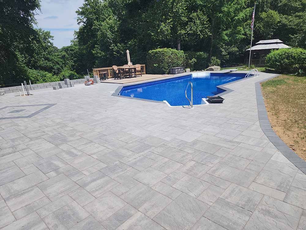 A large swimming pool is surrounded by a patio and trees.