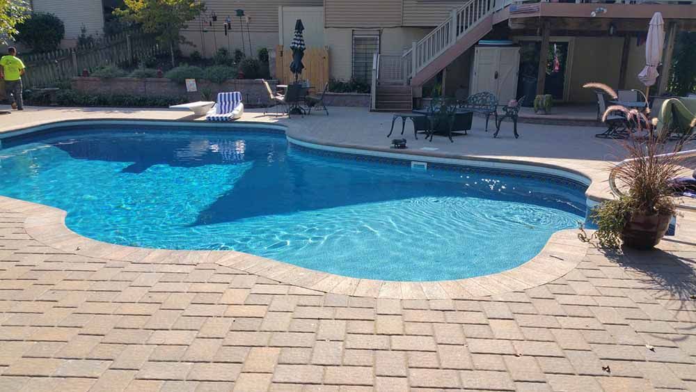 A large swimming pool is surrounded by chairs and umbrellas in a backyard.