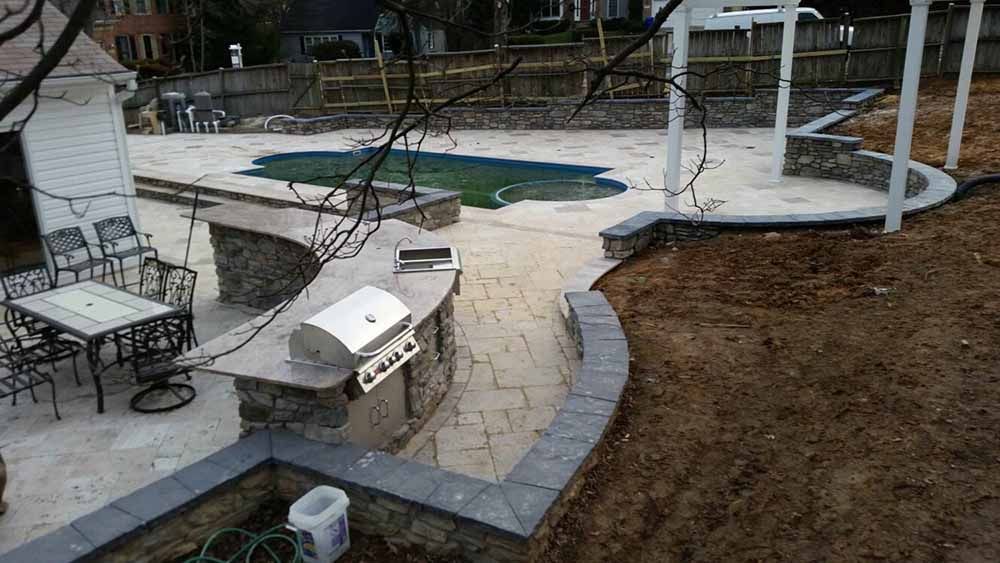 A patio with a grill and a swimming pool in the background.