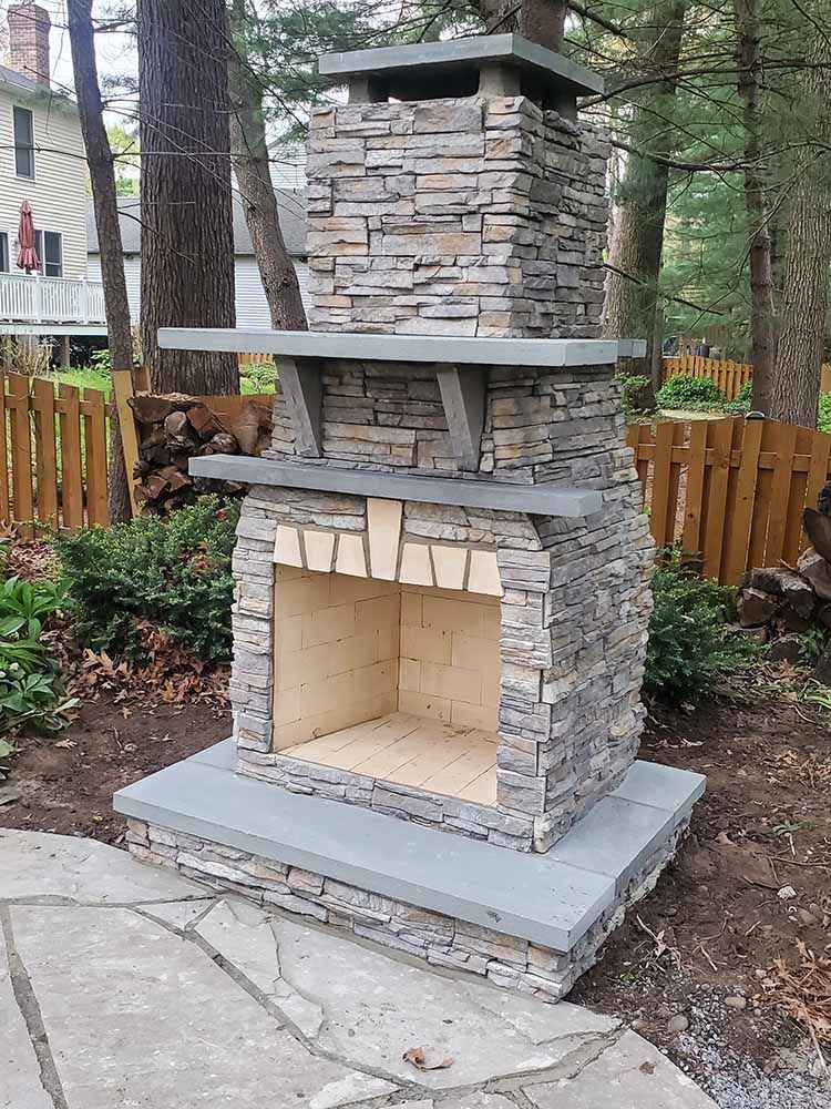 A stone fireplace is sitting on a patio next to a wooden fence.