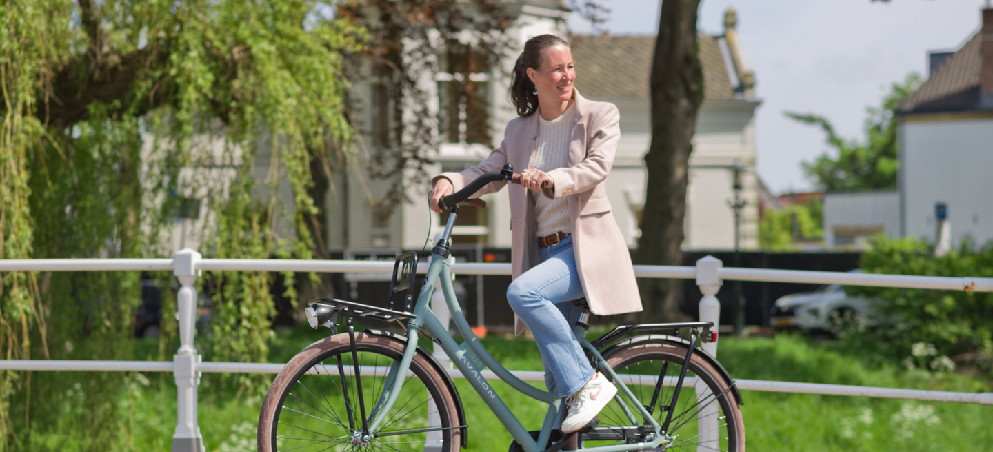 Vrouw fietst ontspannen op een lichtgroene Avalon transportfiets met voordrager langs een gracht