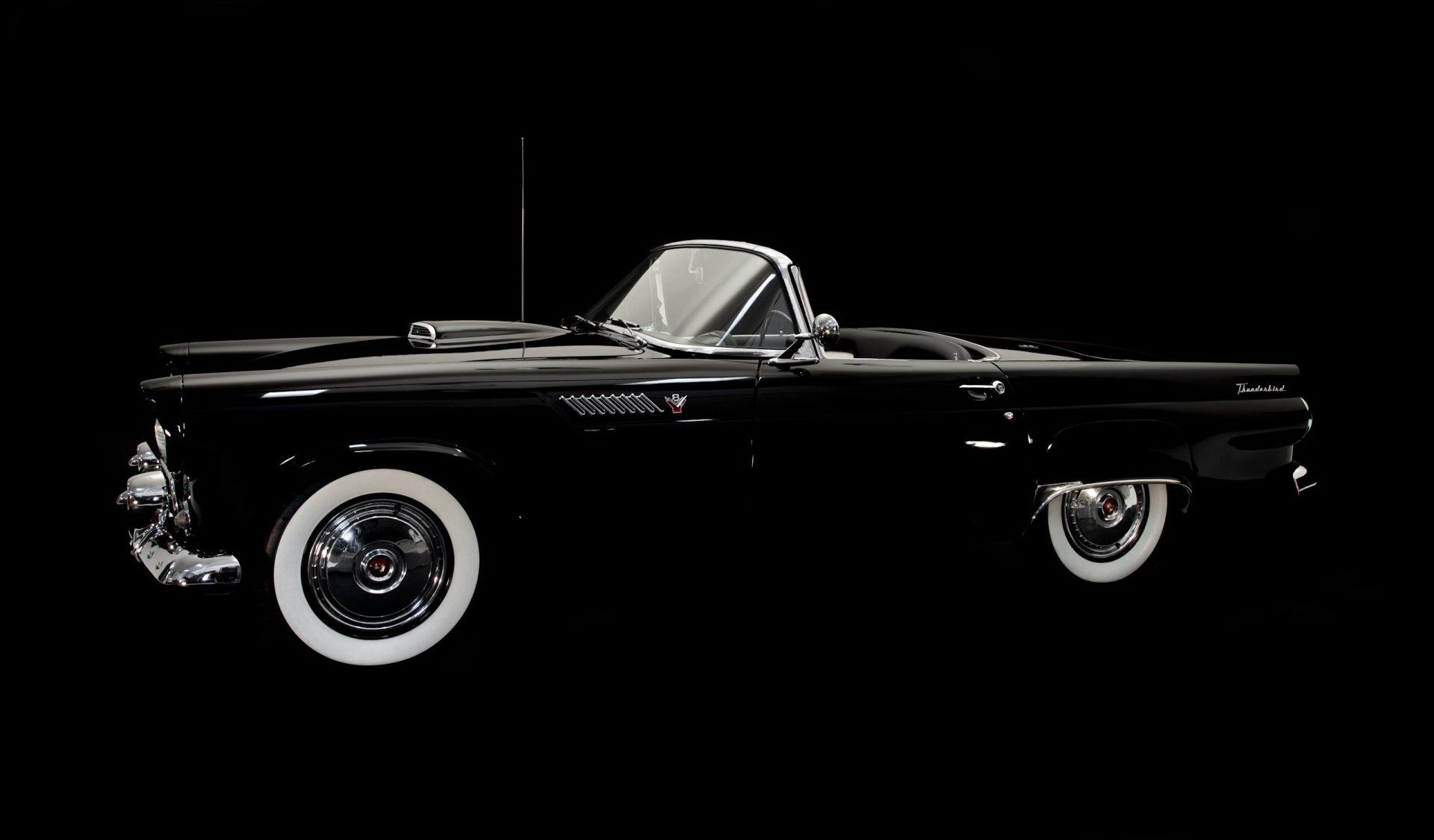 a black convertible car with white tires on a black background .