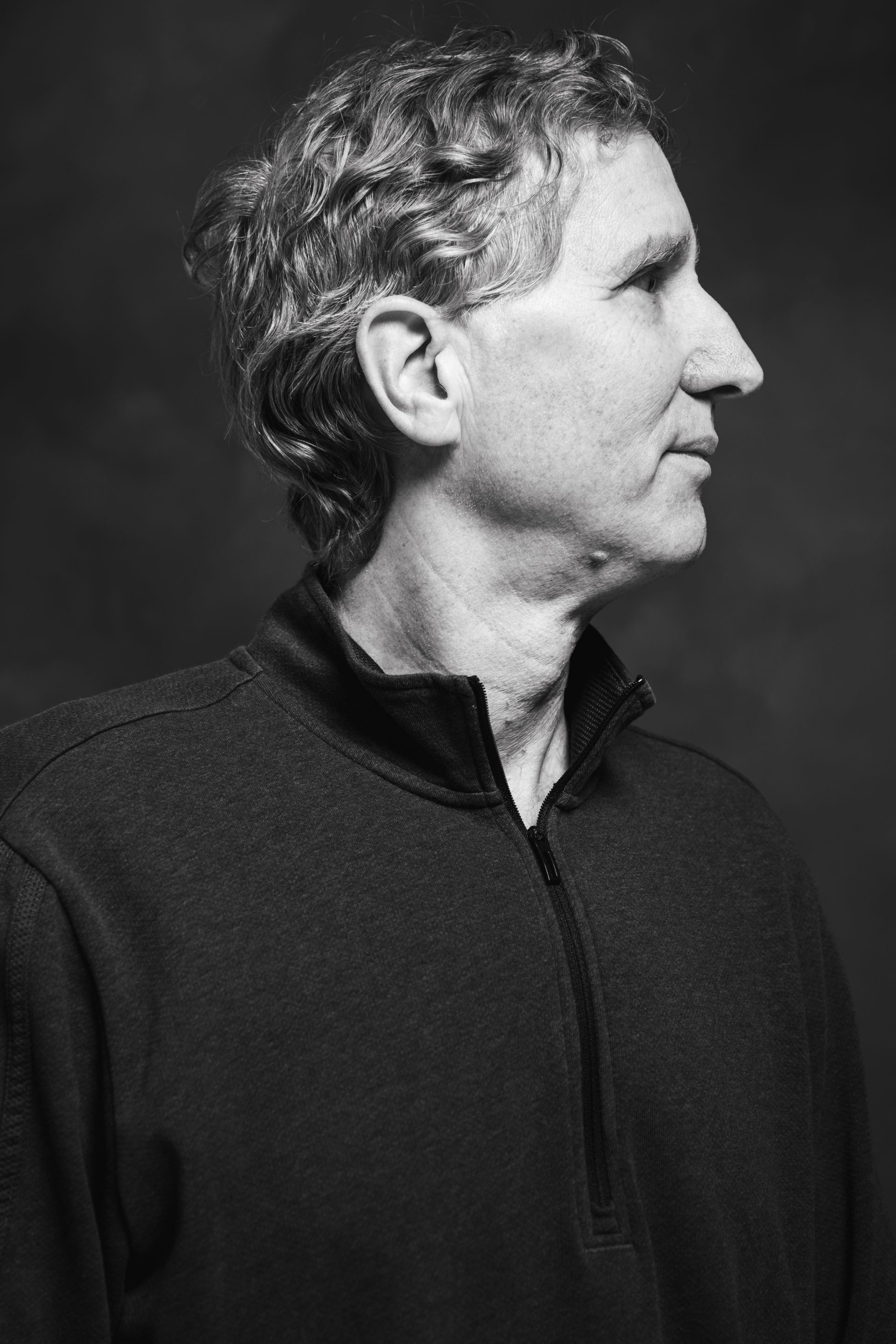 Man with graying hair in profile, wearing a dark sweater; looking to the right.