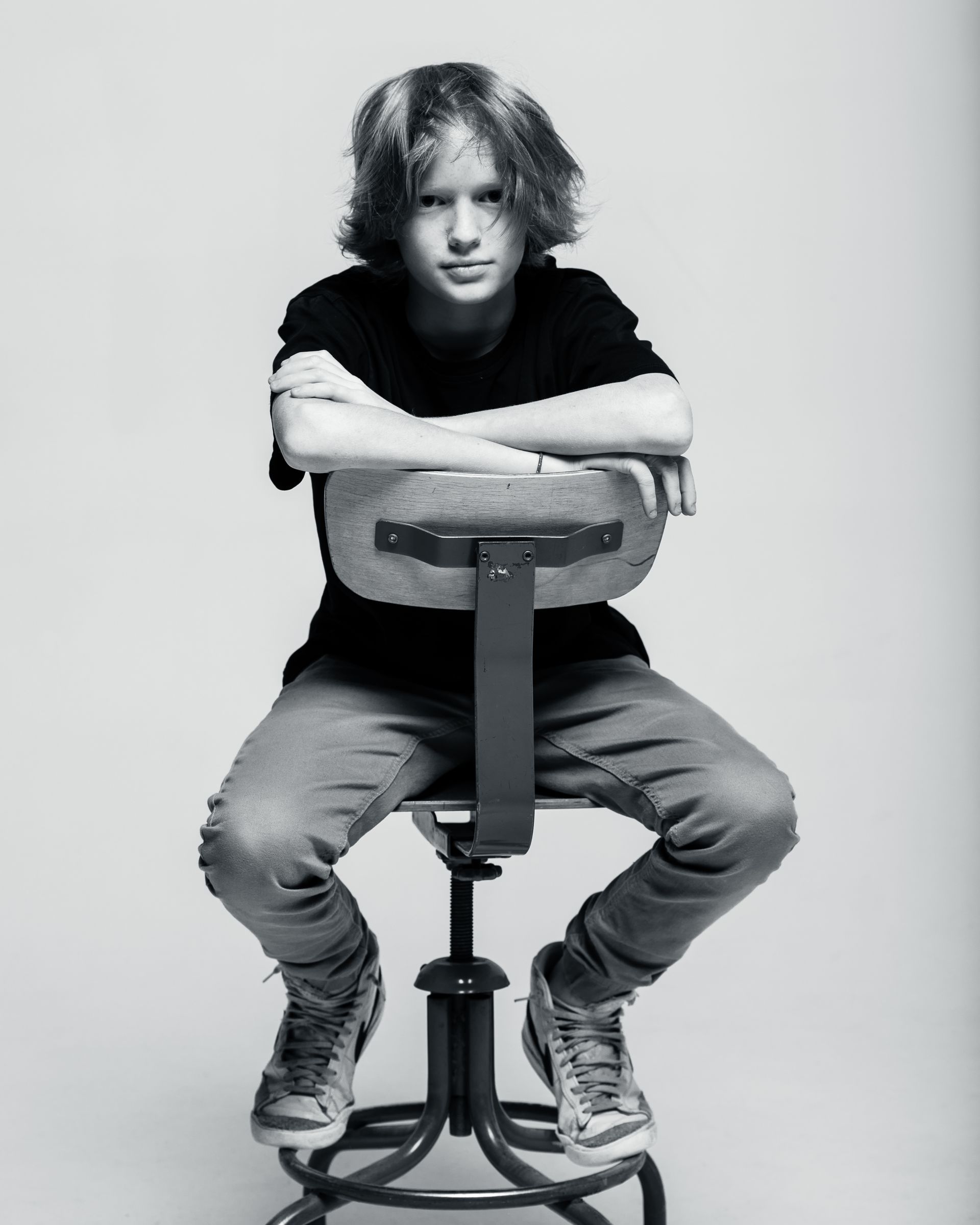 Person with messy hair, arms crossed, seated on a stool, looking at the camera. Black and white.