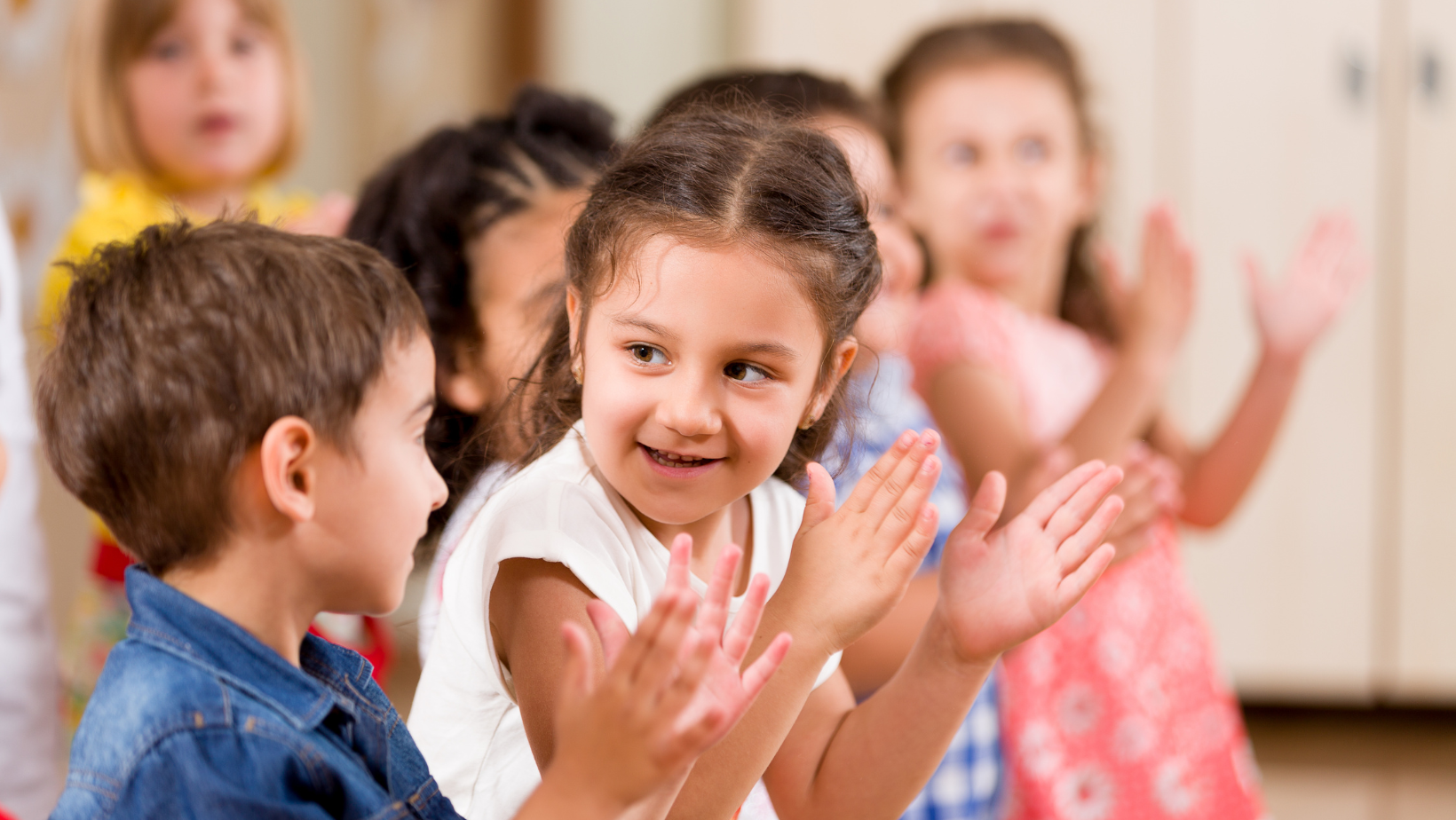 Children clapping and smiling during a group activity in a classroom