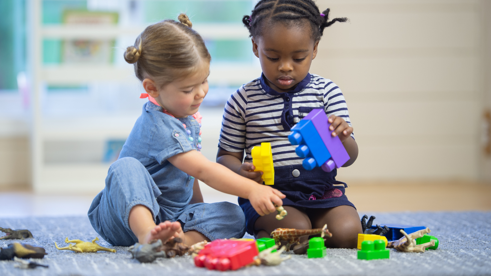 Two children sitting on a carpet, playing with colorful building blocks indoors.