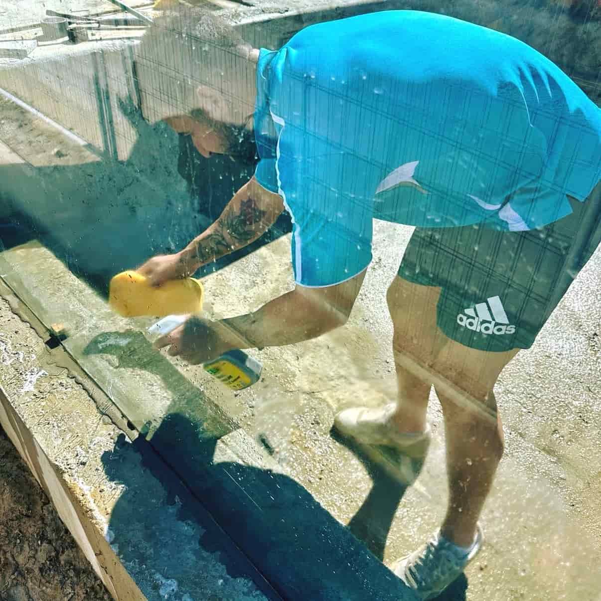 Man in Blue Shirt and Shorts Cleaning a Pool Glass — Glass Pool Windows Australia In Dee Why, NSW