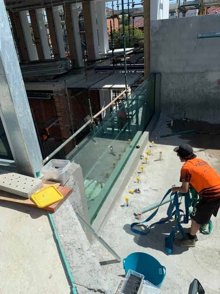 A Man Is Working On A Glass Railing In A Building Under Construction — Glass Pool Windows Australia In Old Bar, NSW