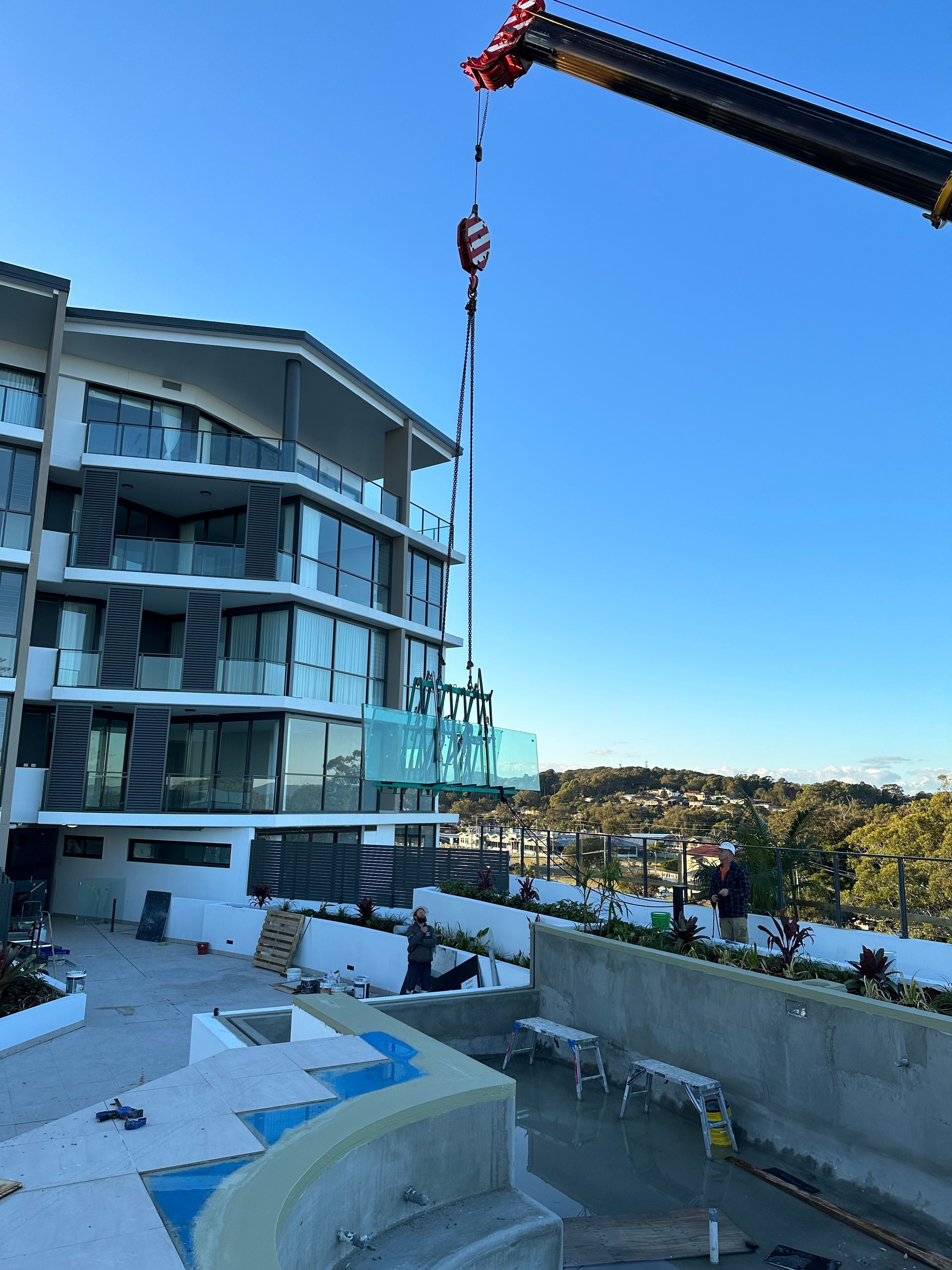 A Crane Is Lifting A Glass Railing In Front Of A Building — Glass Pool Windows Australia In Old Bar, NSW