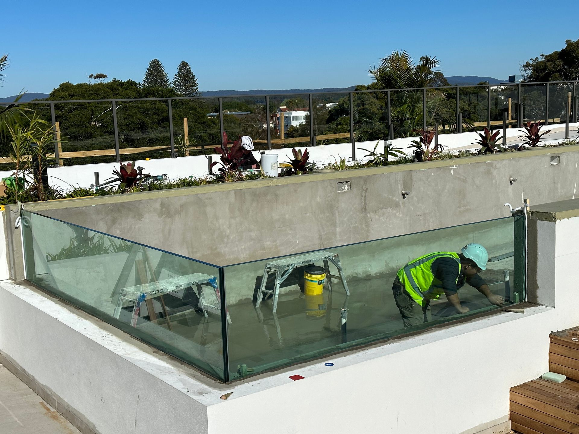 A Man Is Working On A Glass Fence Around A Pool — Glass Pool Windows Australia In Old Bar, NSW