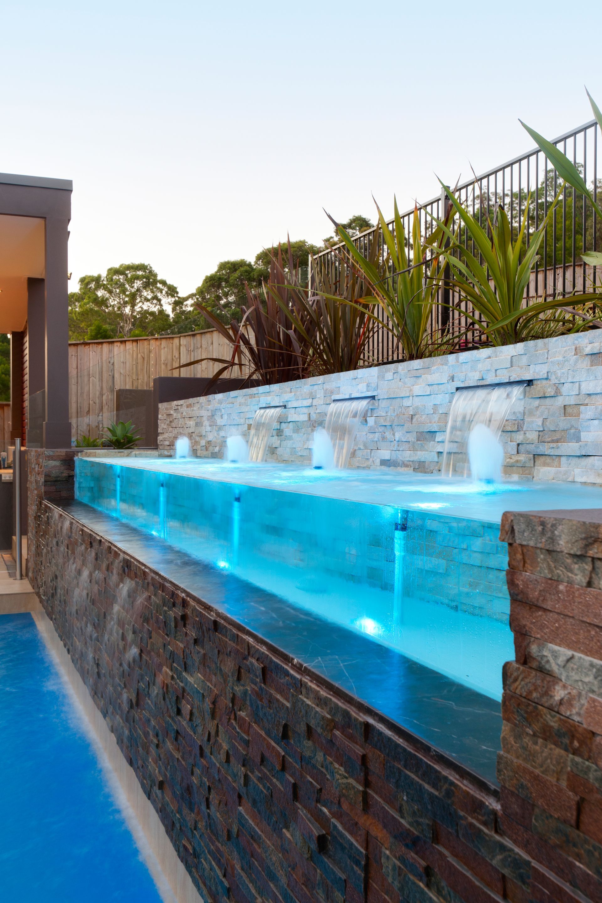 A Swimming Pool With A Brick Wall And A Waterfall In The Background — Glass Pool Windows Australia In Old Bar, NSW