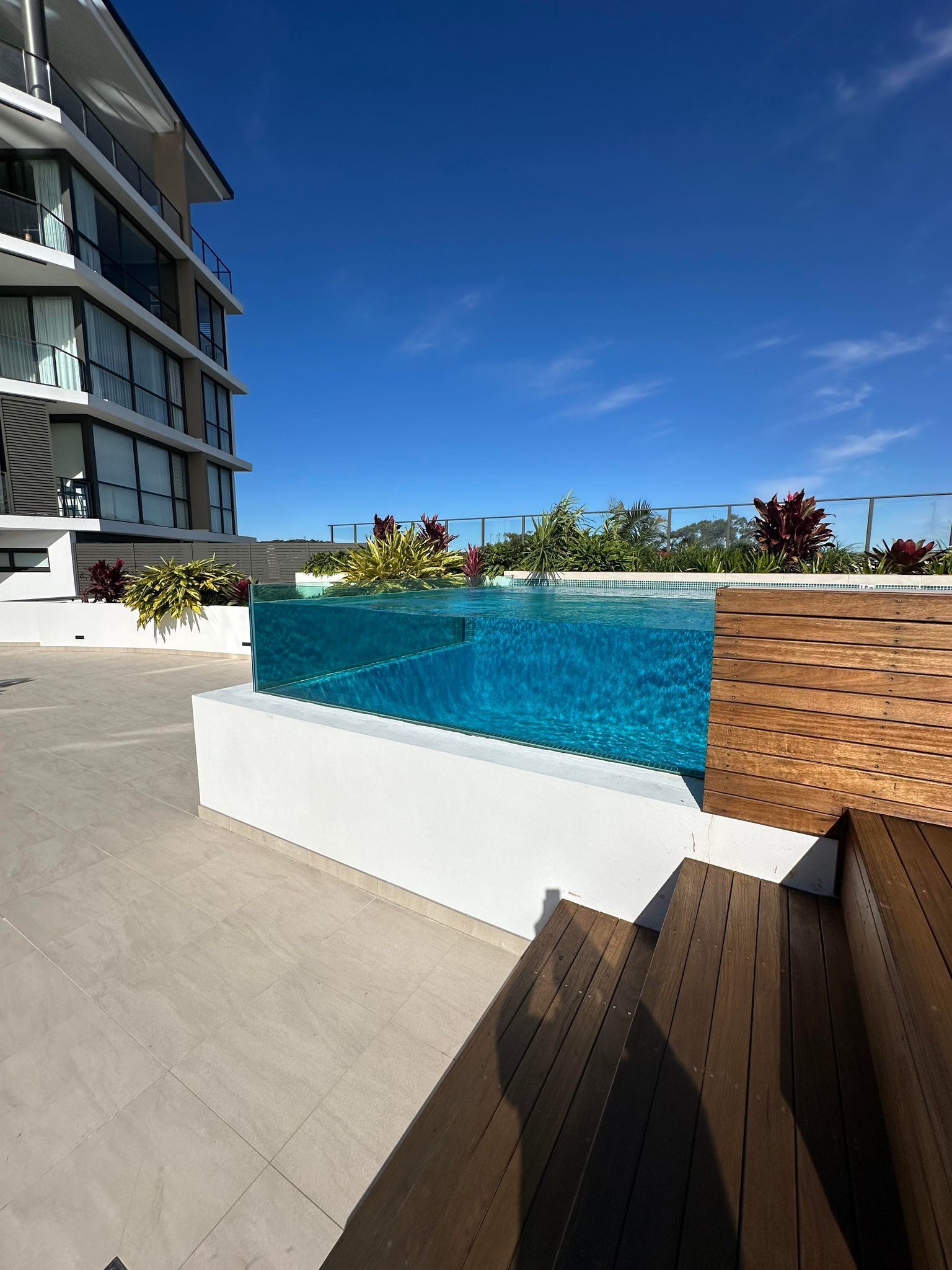 A Large Swimming Pool With A Clear Glass Wall Surrounding It — Glass Pool Windows Australia In Old Bar, NSW