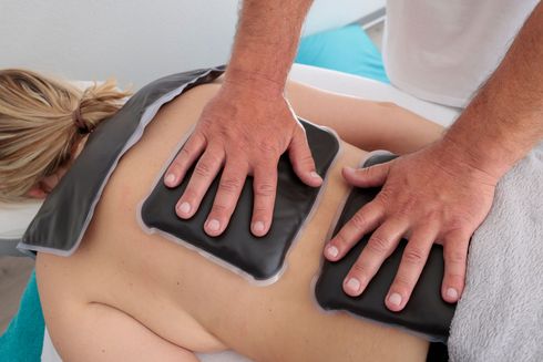 Therapeutin legt während einer Massage heiße Steinpackungen auf den nackten Rücken einer Person