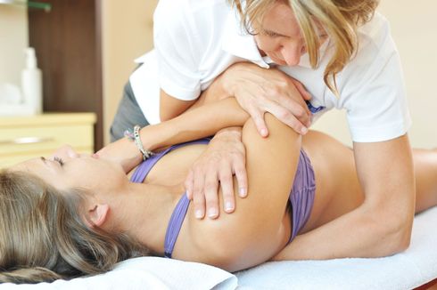 Eine Frau erhält in einem hellen Spa-Raum auf einer Behandlungsliege eine Schultermassage