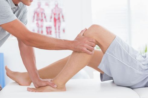 Ein Physiotherapeut dehnt das Bein eines Patienten auf einer Behandlungsliege in einer hellen Praxis
